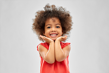 A child with a big smile holding her chin in her hands